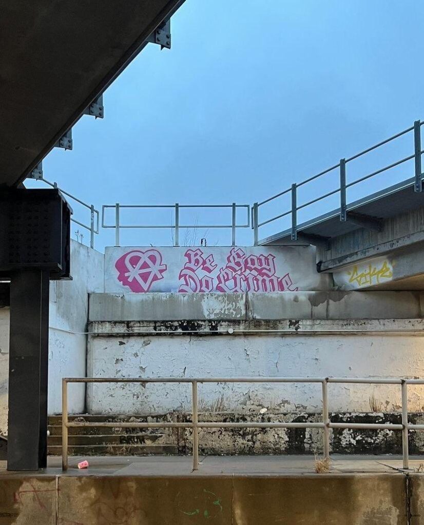pink graffiti on wall, heart circle A and text saying be gay do crime